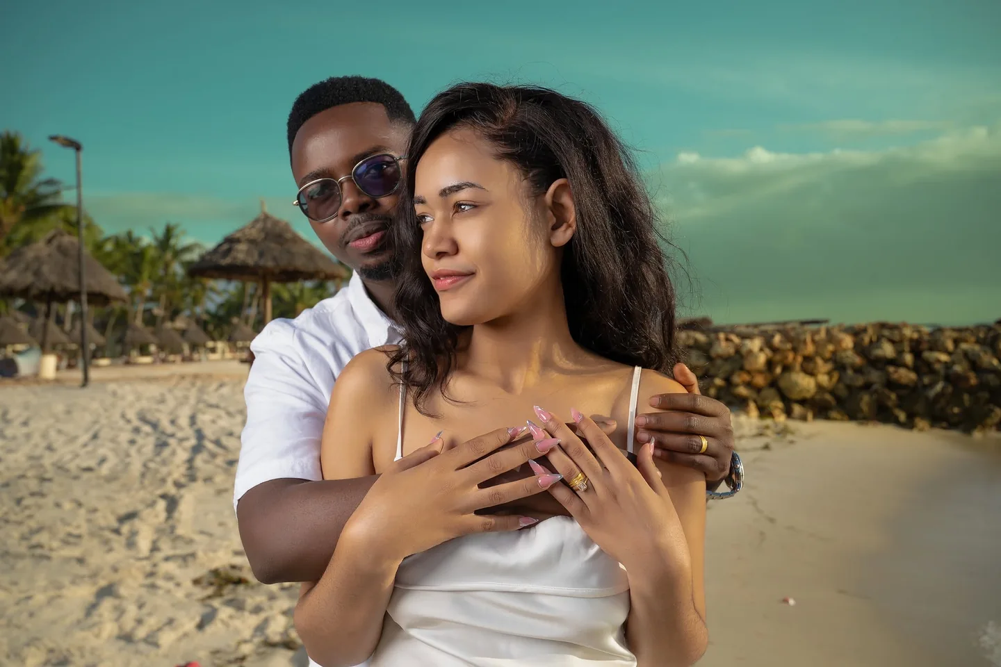 Couple embracing on a beach, with their hands together and rings visible