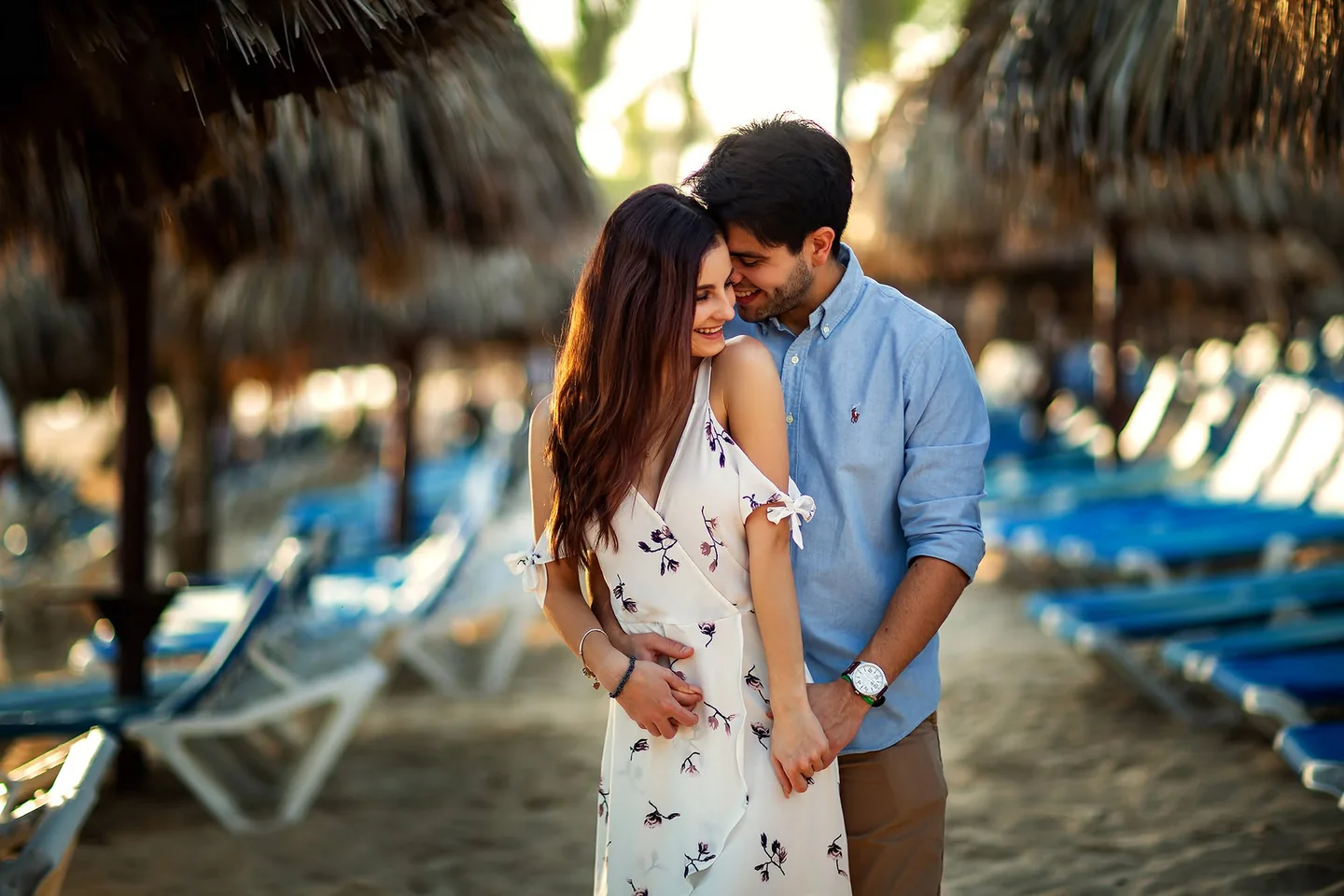 Couple smiling at one another beside blue beach loungers
