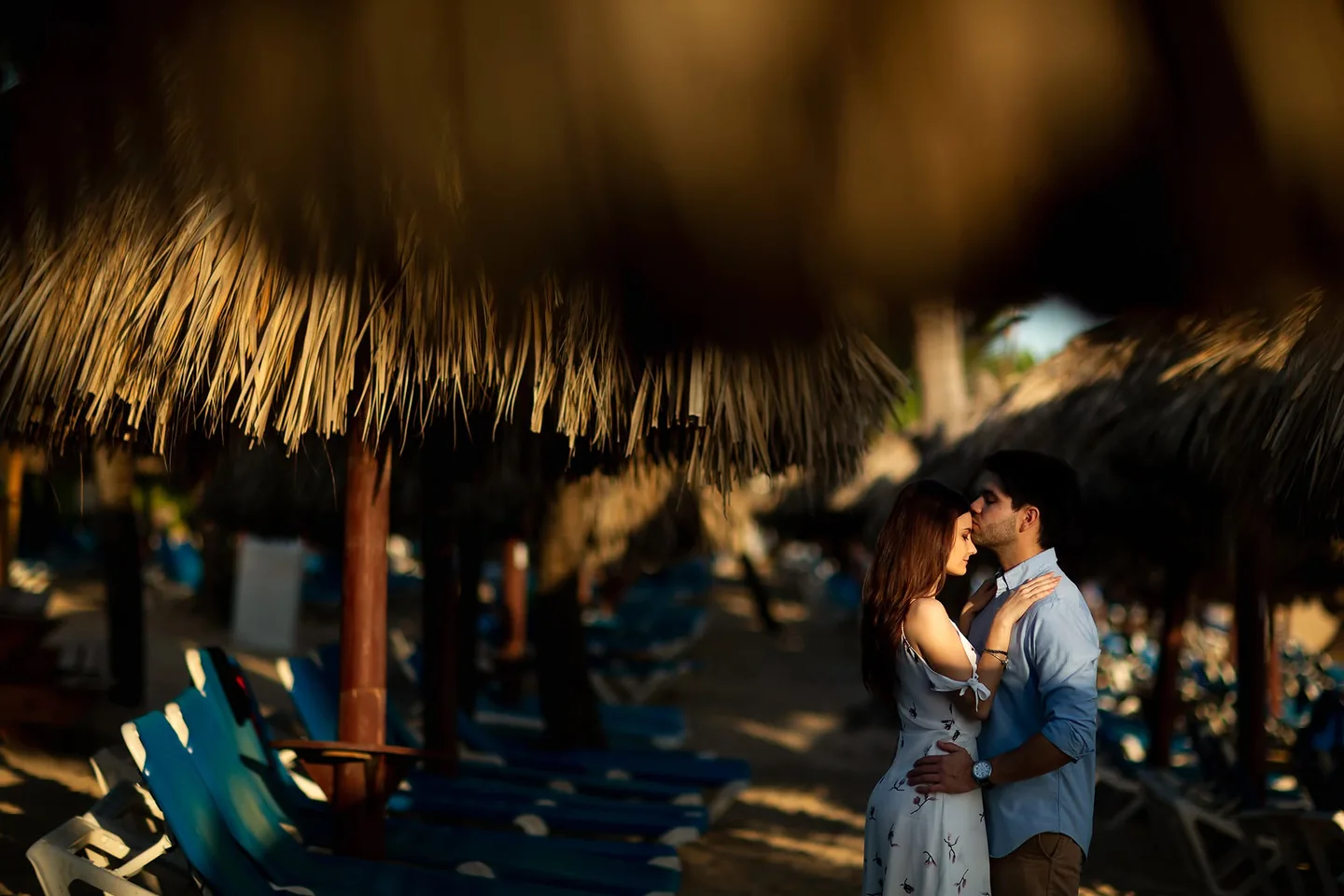 Couple sharing a kiss, framed by the shade of a thatched beach shelter