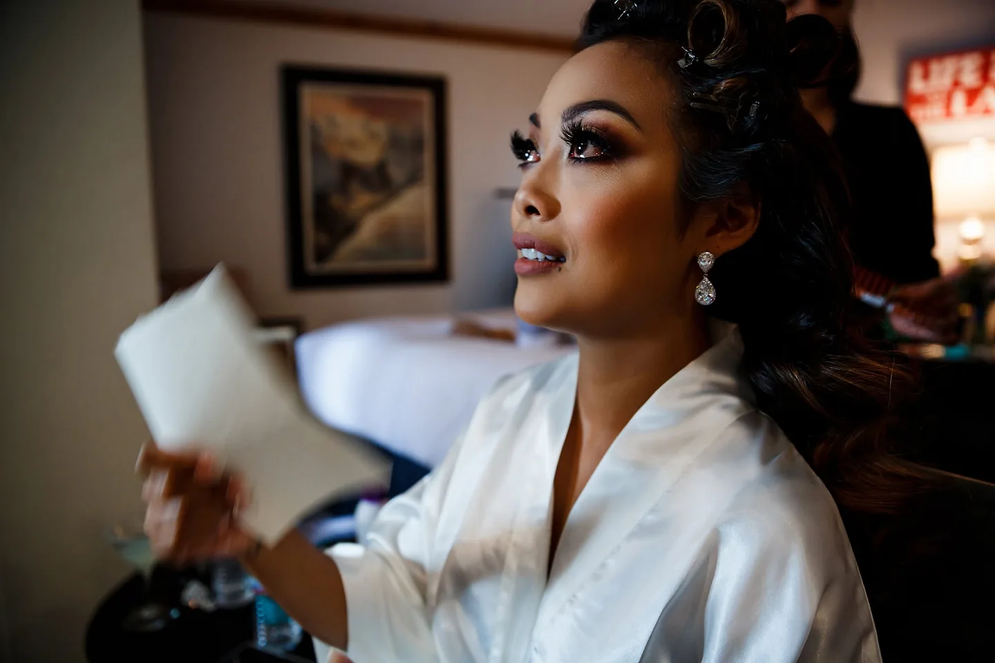 Bride in a white robe looking towards the window while her hair is styled