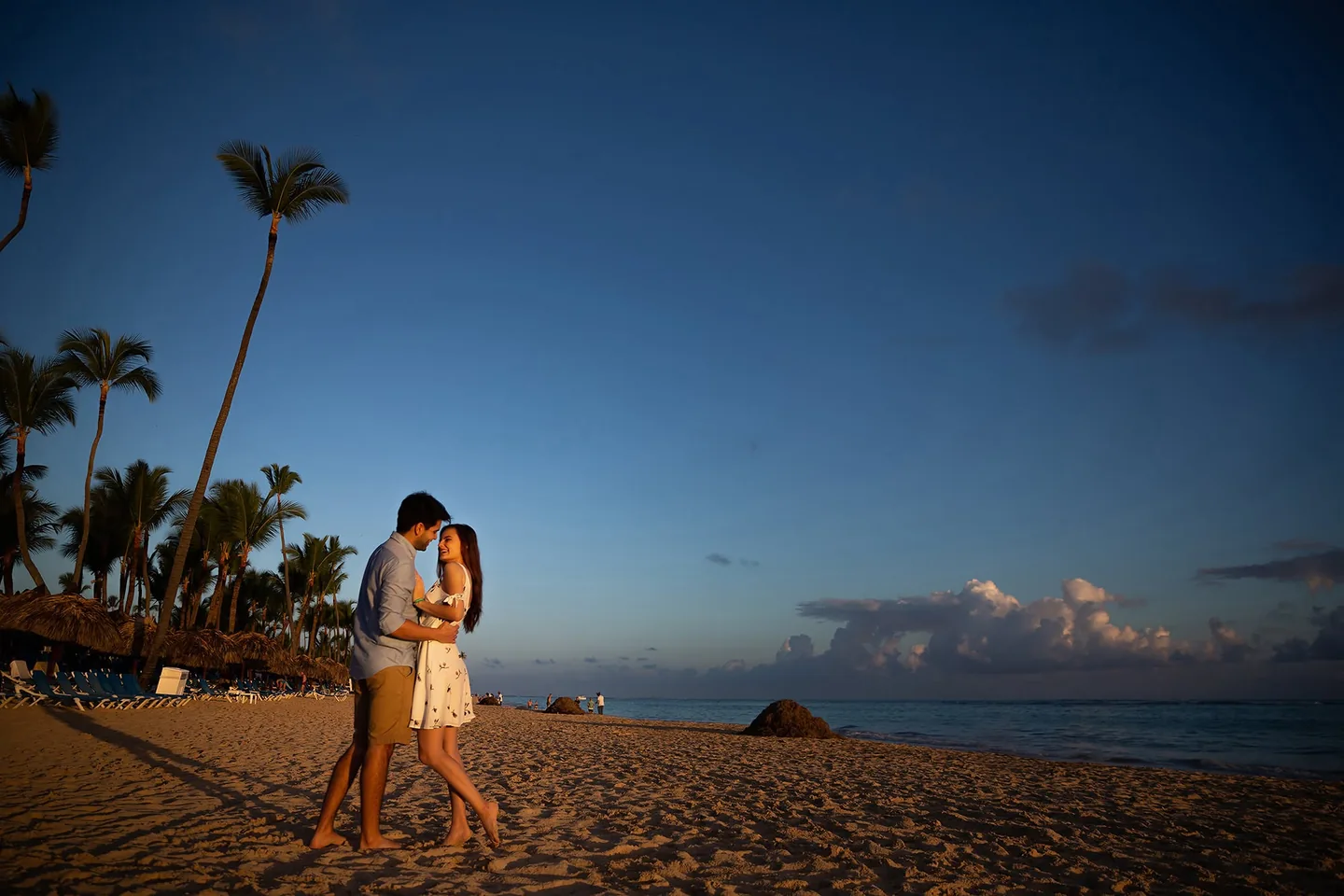 Couple embracing on a wide sandy beach beneath tall palm trees
