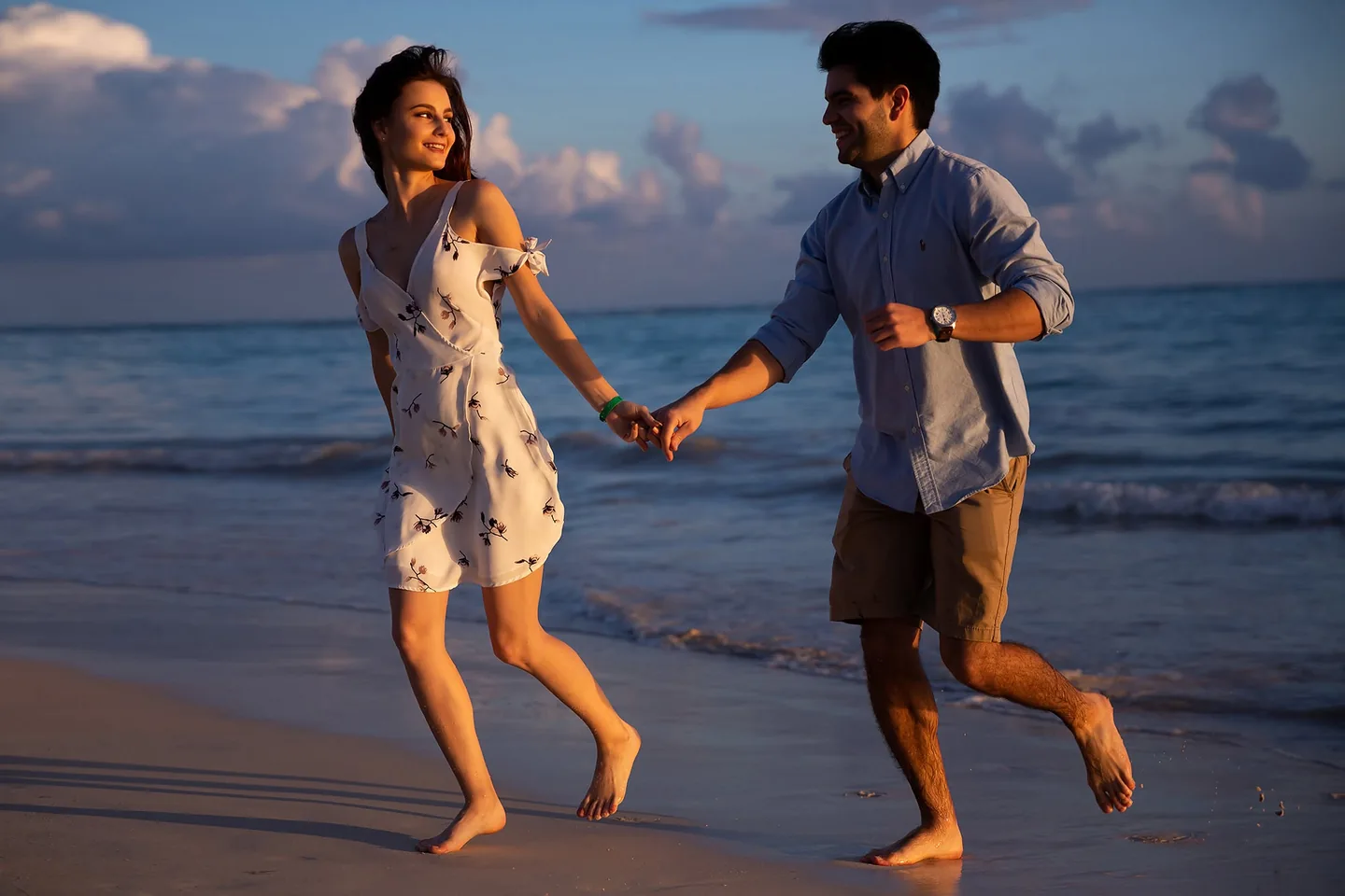 Couple running hand in hand at the water’s edge in warm evening light
