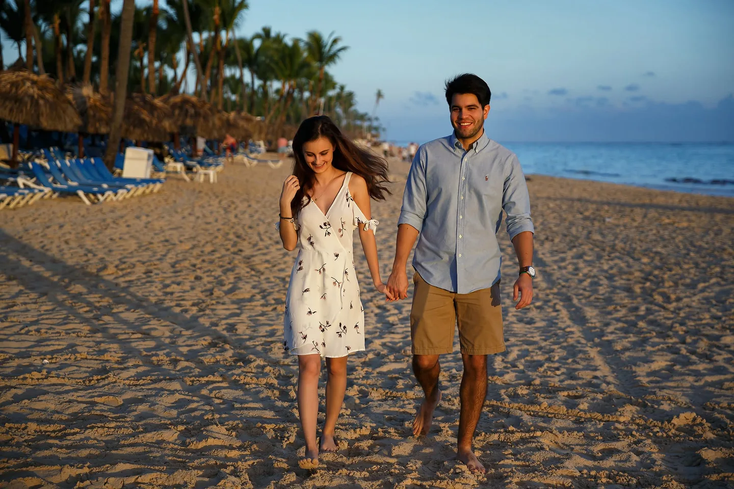 Couple walking barefoot and holding hands along a palm-lined beach