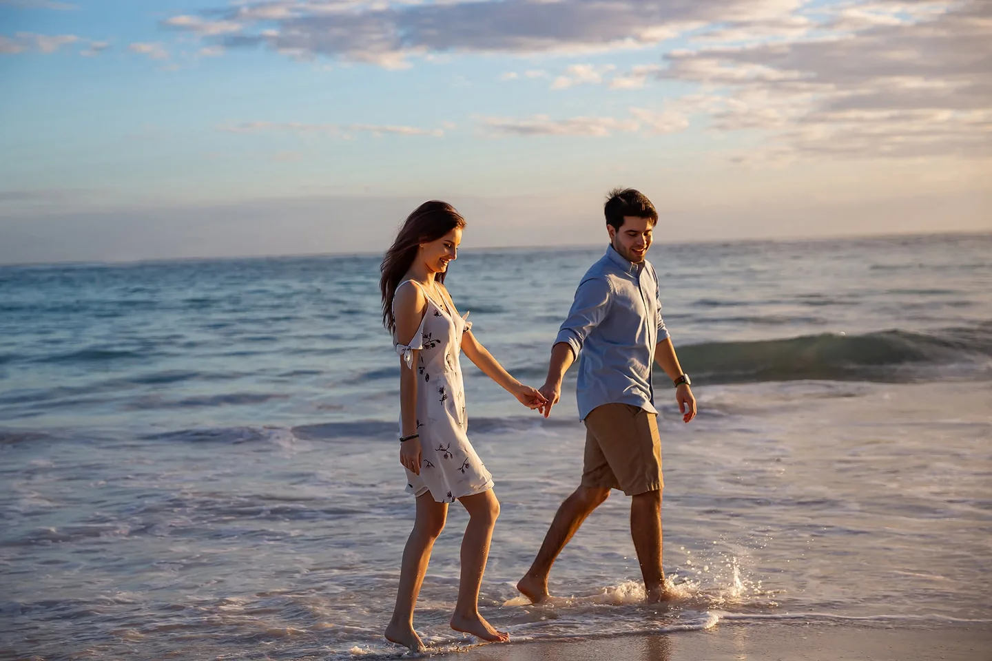 Couple holding hands as they walk through shallow waves at sunset