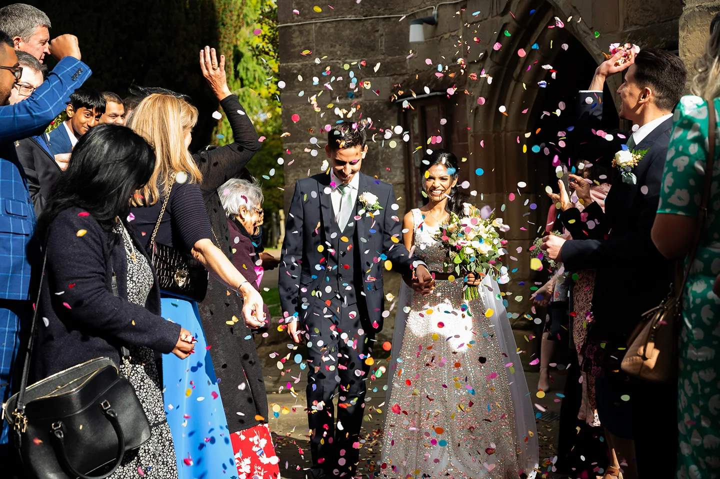 Smiling newlyweds leaving a church as guests shower them with confetti