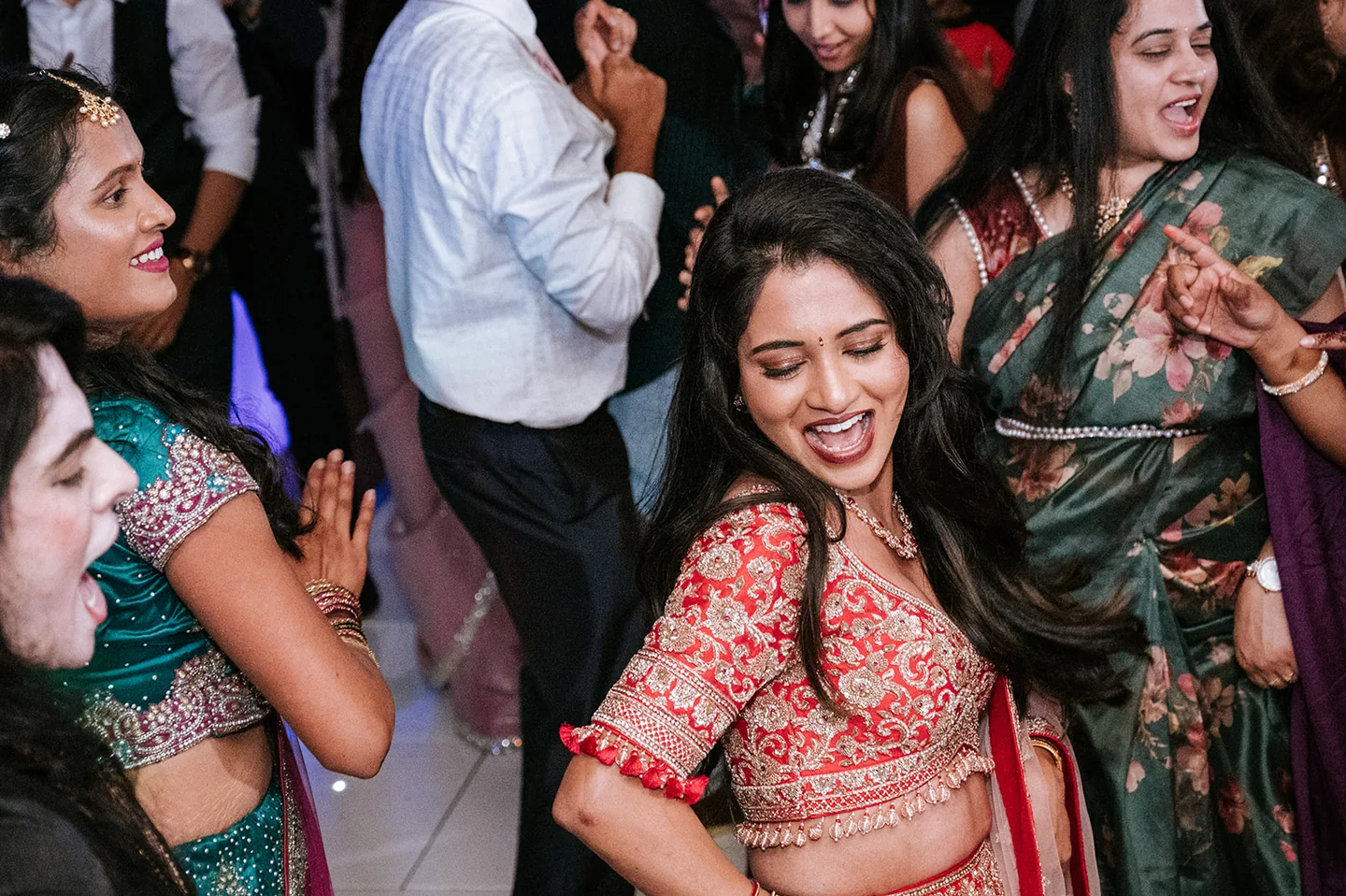 Bride in an embroidered red outfit dancing among friends at the reception
