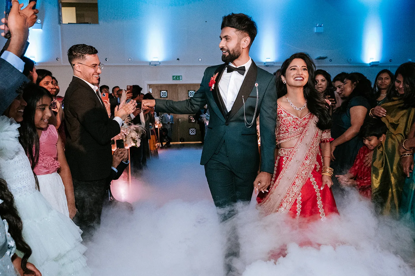 Wedding couple entering their reception through mist as guests applaud