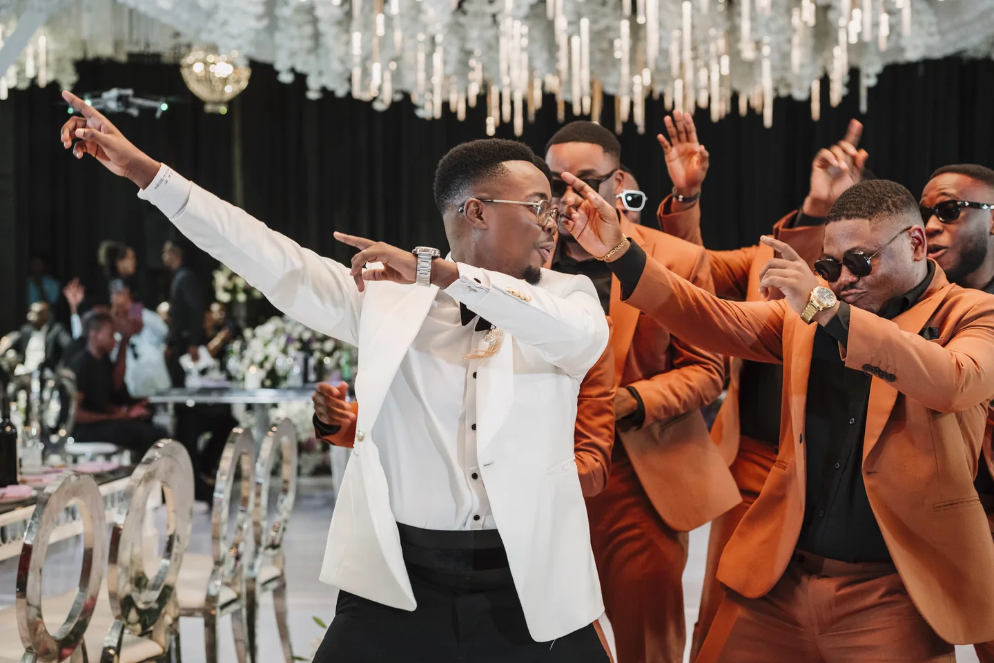 Groom in a white dinner jacket dancing with groomsmen in orange suits