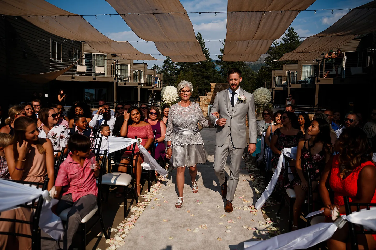 Groom walking arm in arm with a family member between rows of wedding guests