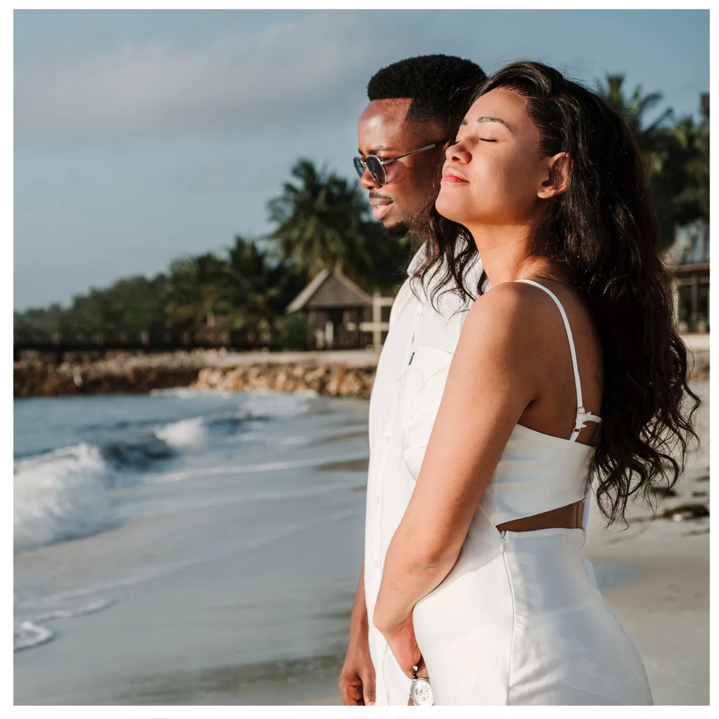 Couple standing close together in the sunlight beside the sea
